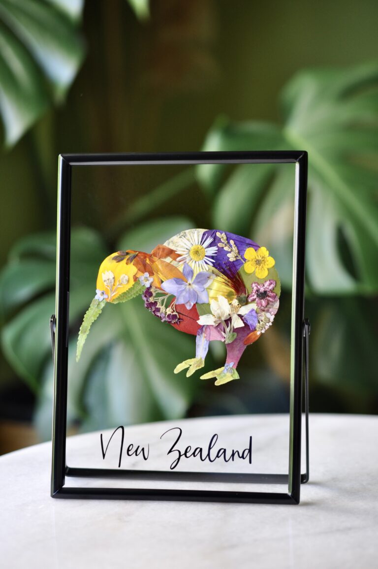 Pressed flower artwork of a Kiwi bird in a black frame, with the label "New Zealand" underneath.