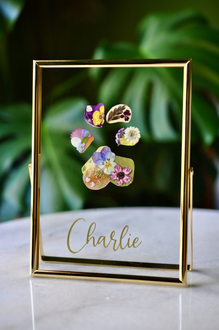 Dog paw print made from real pressed flowers in a gold glass frame with the name “Charlie.”