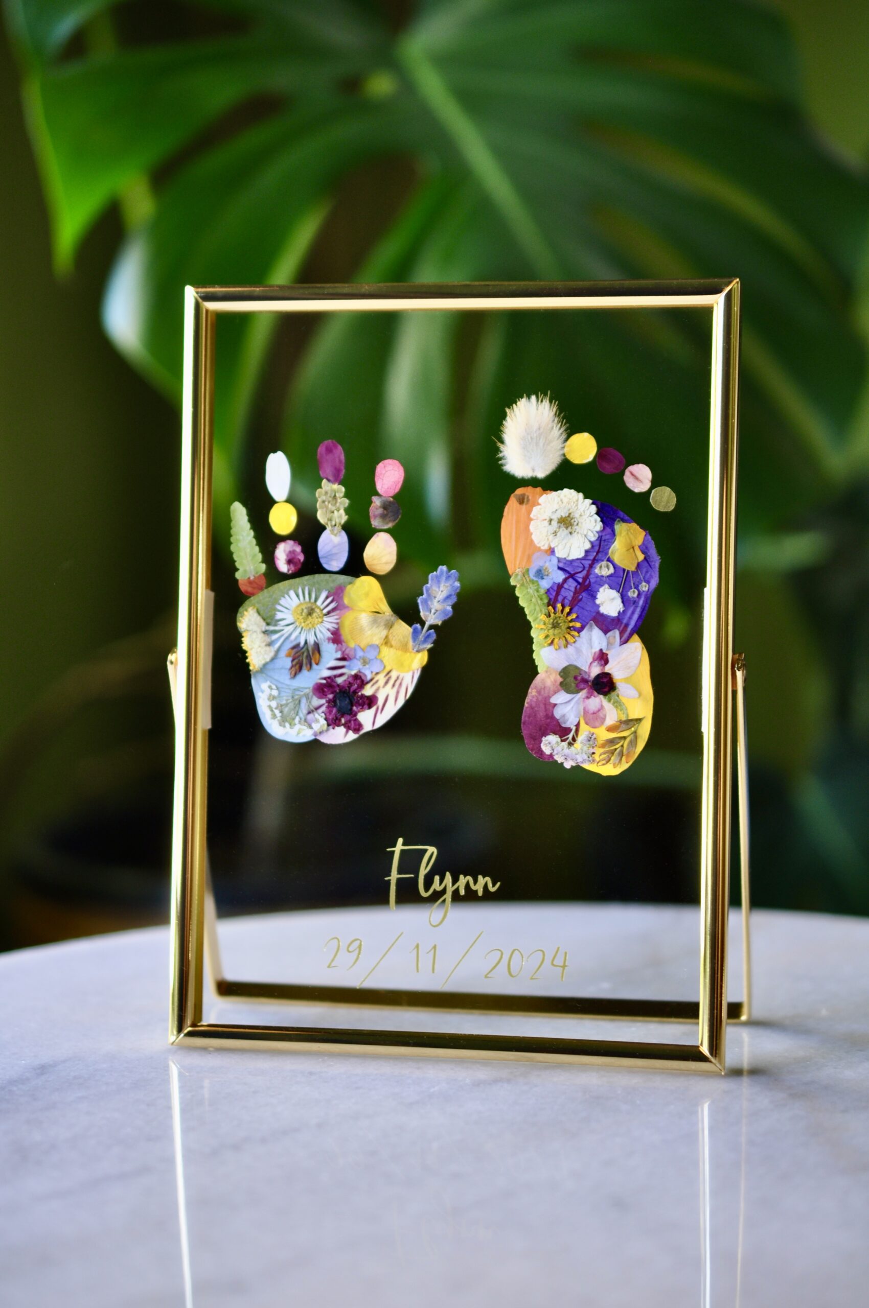 Personalised baby hand and footprint made from real pressed flowers with the name Flynn and birth date.