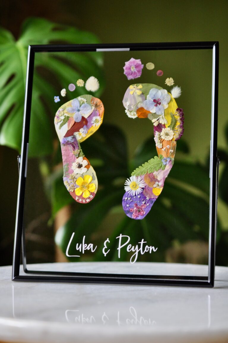 Sibling baby footprints made from real pressed flowers in a double glass frame with names "Luka & Peyton" beneath.