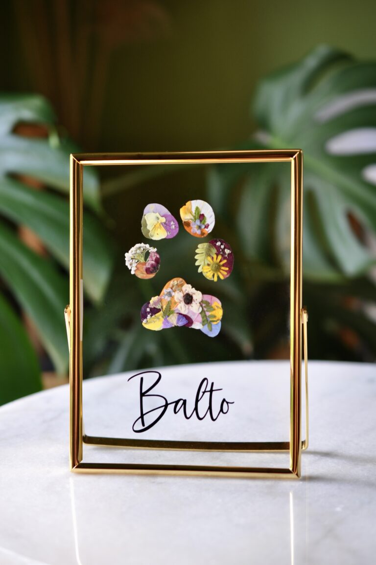 Dog paw print made from real pressed flowers in a gold glass frame with the name “Balto.”