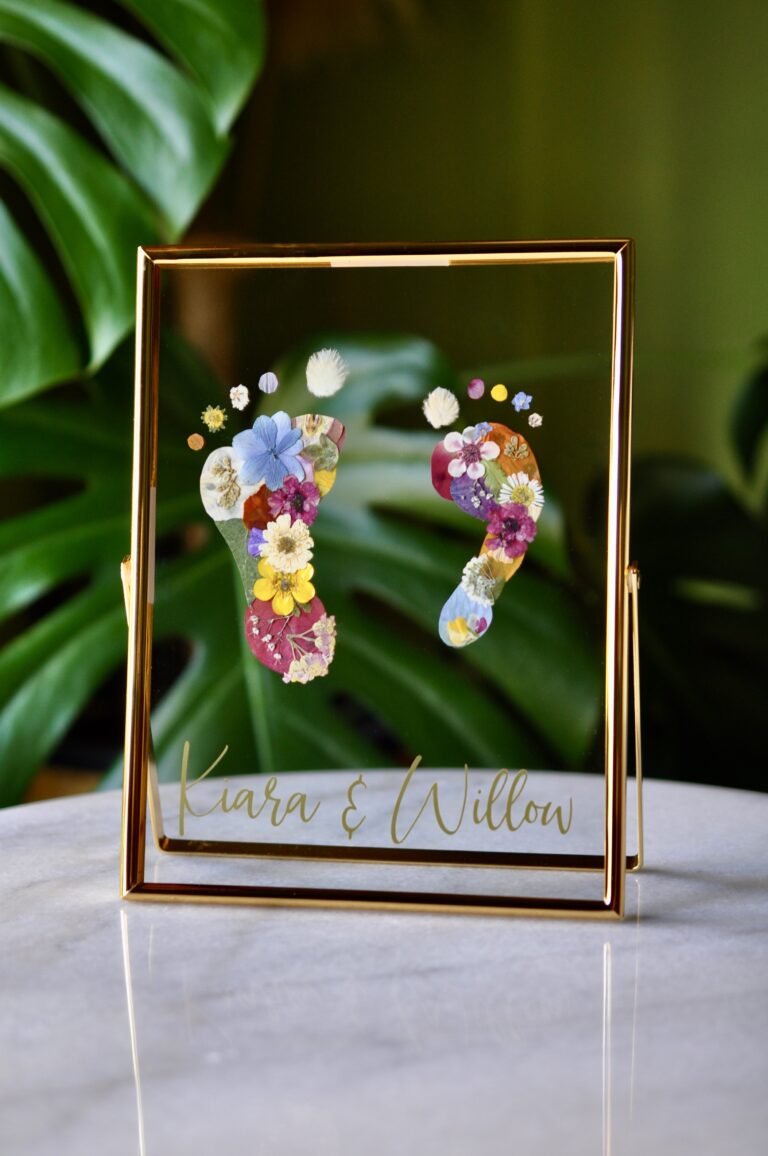 Sibling baby footprints made from real pressed flowers in a double glass frame with names "Kiara & Willow" beneath.