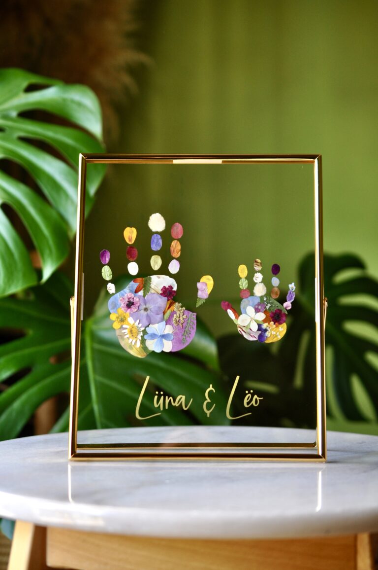 Framed sibling handprints made from real pressed flowers with the names Lüna and Leo, set in gold glass frame.