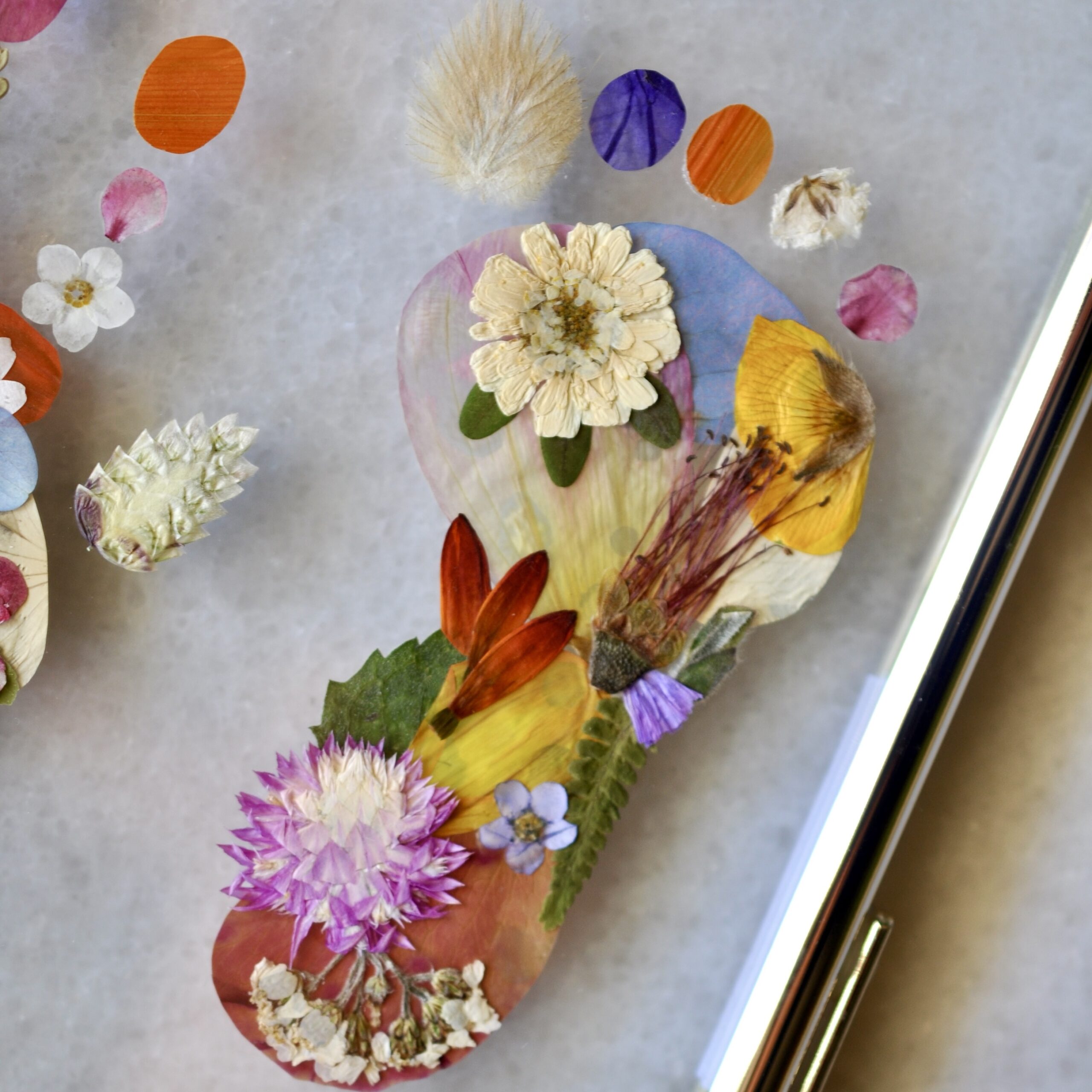 Gold double glass frame displaying a baby’s tiny hand and footprint made from real pressed flowers, with the name “Roen” in gold lettering
